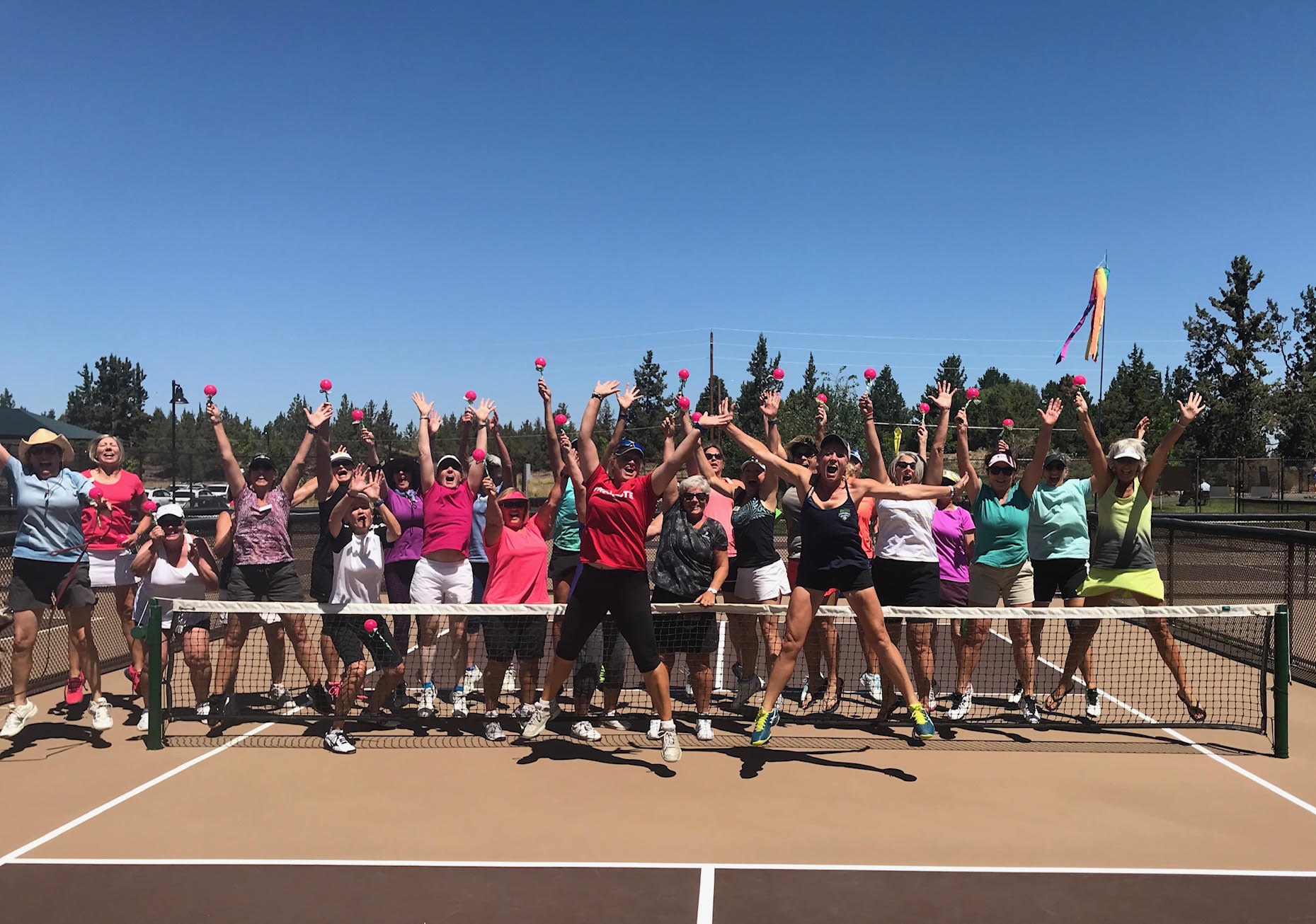 A large group of players celebrating with paddles raised at the end of a pickleball clinic